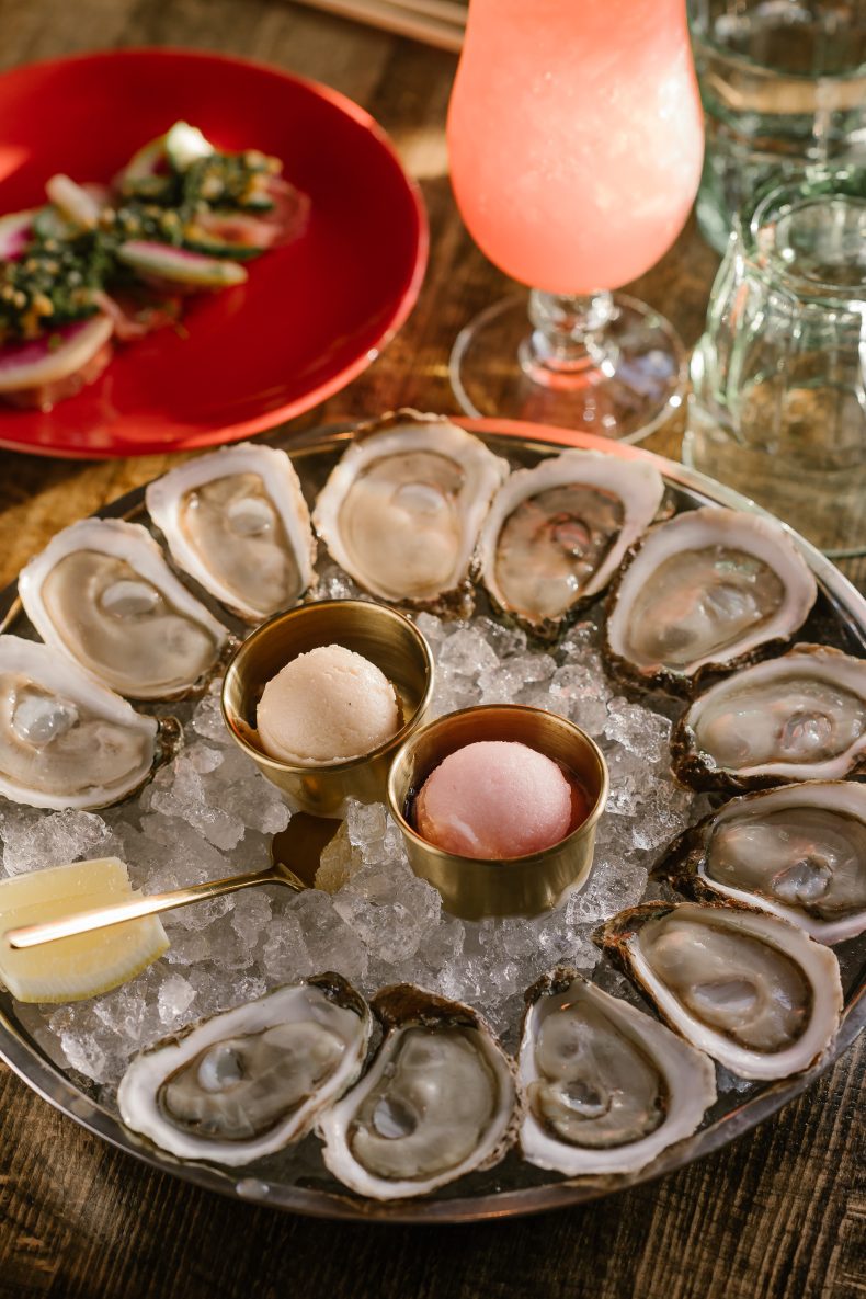 Platter of oysters on ice with mignonette, next to a frozen pink cocktail