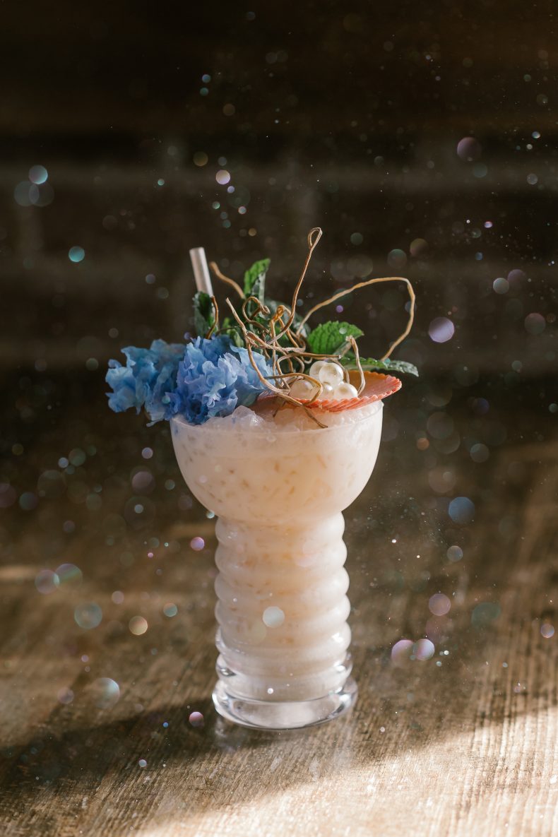 Frozen tropical cocktail garnished with blue flowers, pearls and a seashell