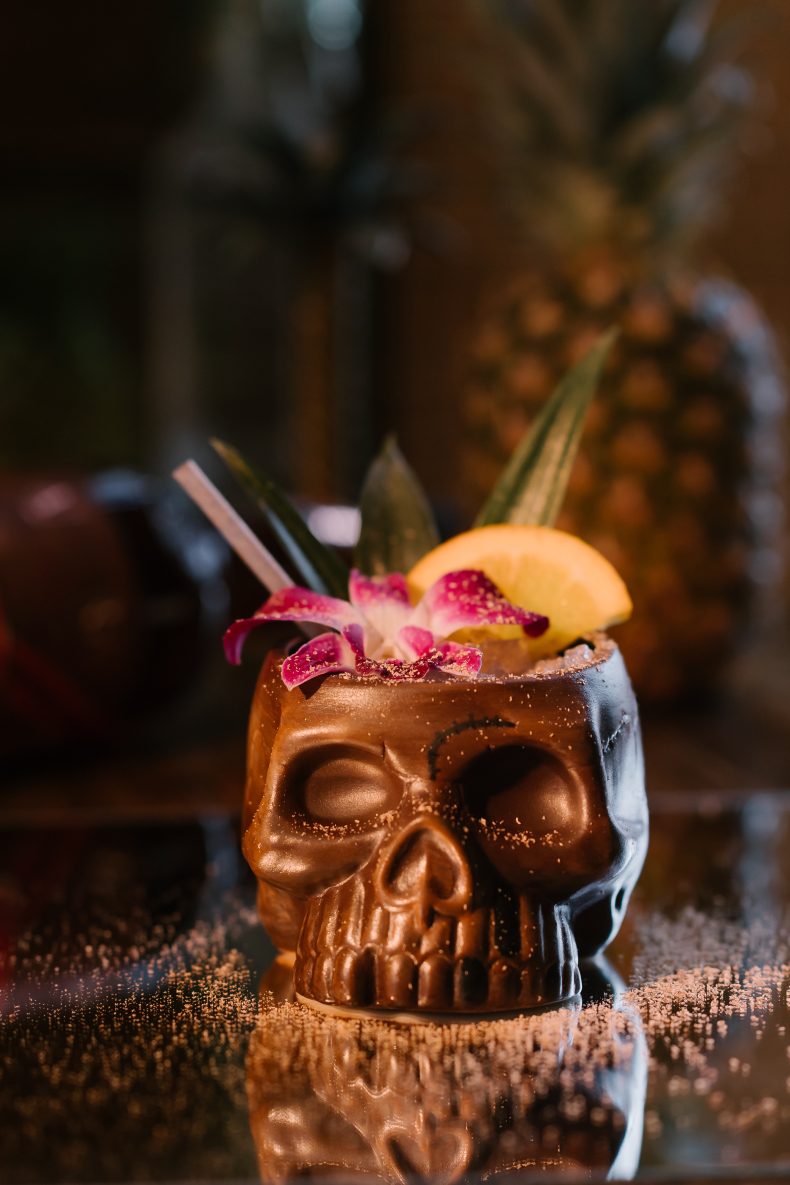 Rum cocktail in a copper skull mug with an orchid and citrus garnish